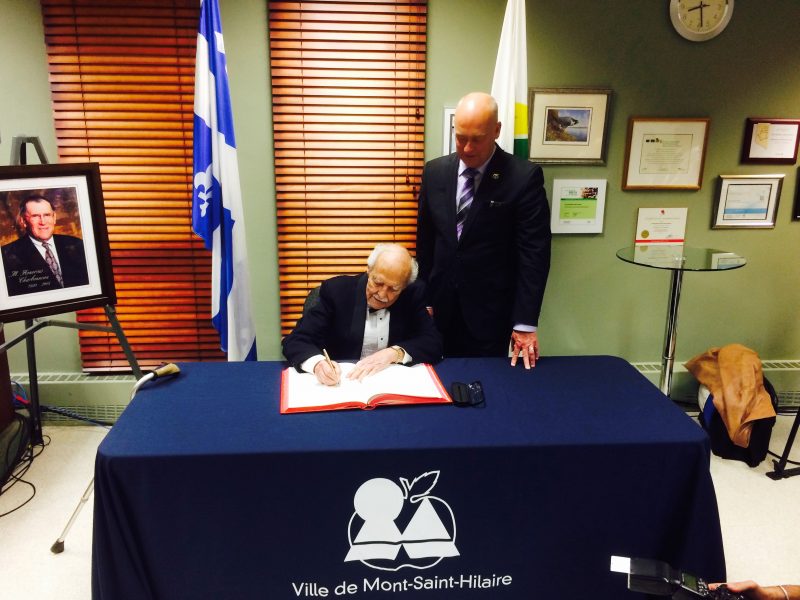 L'ancien maire Jean-Guy Sénécal signant le livre d'or de la municipalité en compagnie du maire actuel Yves Corriveau .