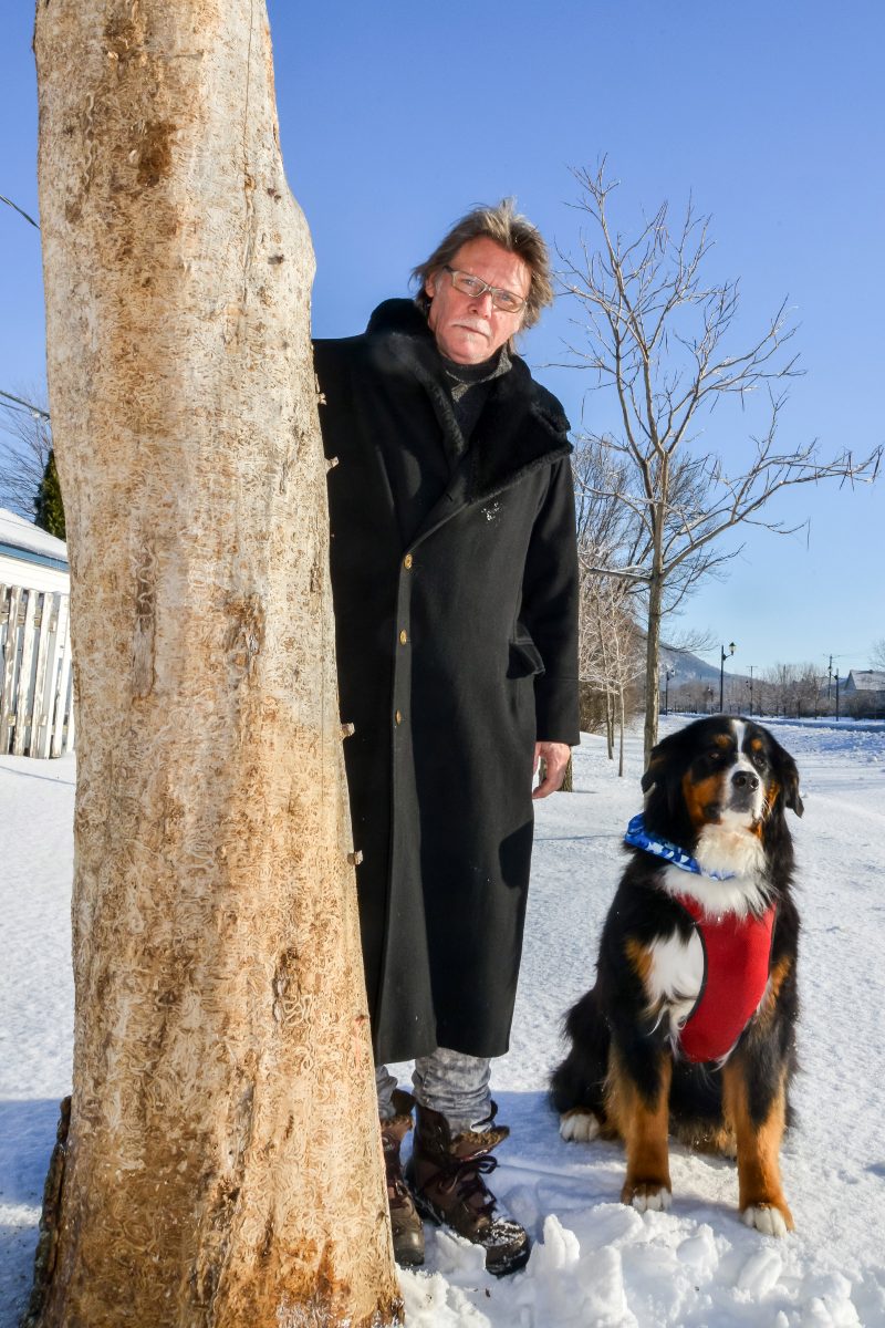 Daniel-Vincent Bernard, en compagnie de son chien Amos, à côté d'un des arbres qu'il sculptera très prochainement au bord de la rue Saint-Jean-Baptiste à Belœil.Photo: François Larivière