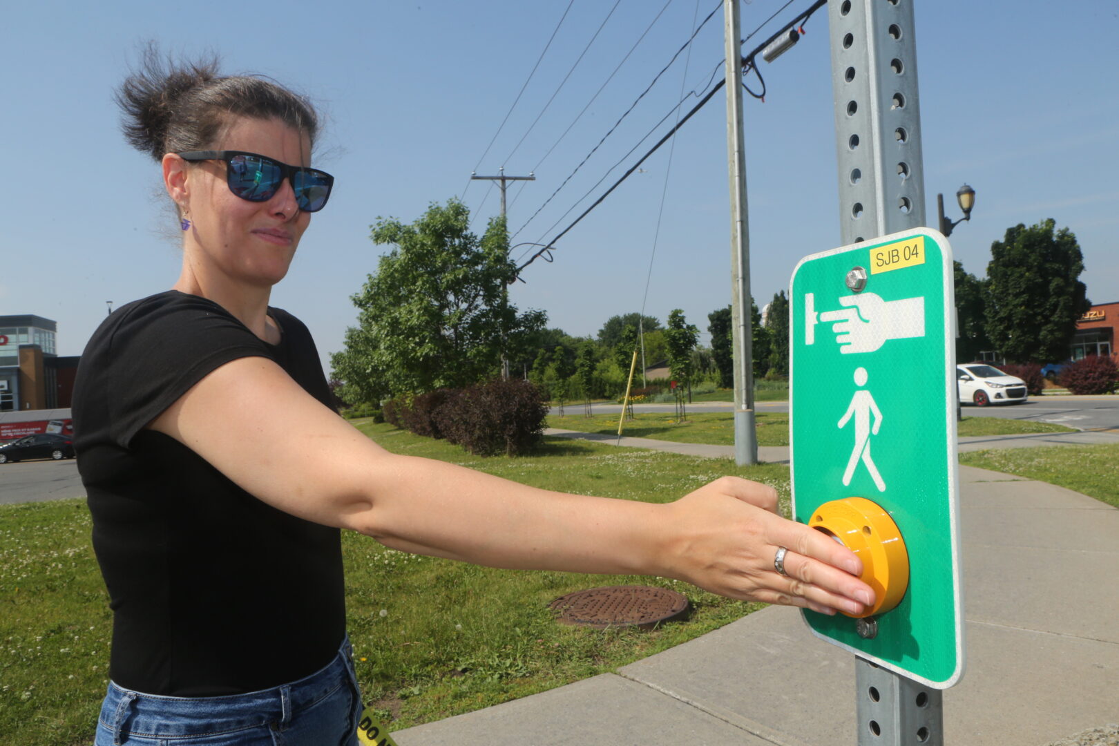 Claudia Nigrelli activant le panneau lumineux qui se trouve à une dizaine de pieds d’une traverse piétonne au carrefour giratoire Yvon-L’Heureux/Saint-Jean-Baptiste. Photo Robert Gosselin | L’Œil Régional ©
